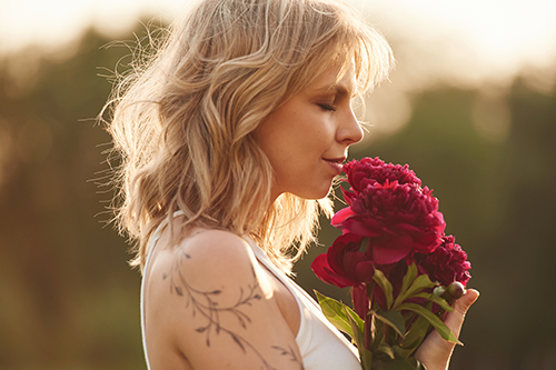 Side view. Beautiful young woman is standing outdoors and holding red flowers